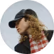 Person wearing a black cap, sunglasses, and a red plaid scarf with curly hair.