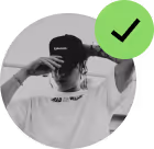Person wearing a black cap and white shirt, partially covering face with hand, green checkmark overlay.