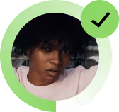 Dark-skinned person with short curly hair wearing a white shirt and a green verified check mark badge