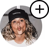 Woman with curly hair wearing a cap making a fish face expression with a plus icon overlay.