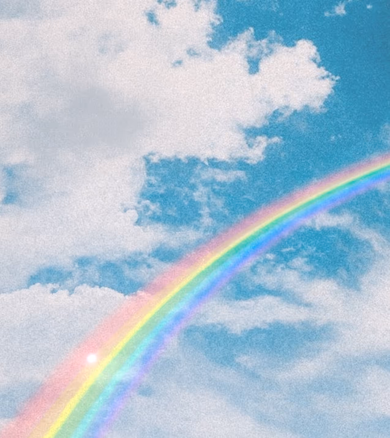 Bright rainbow arching across a partly cloudy blue sky.
