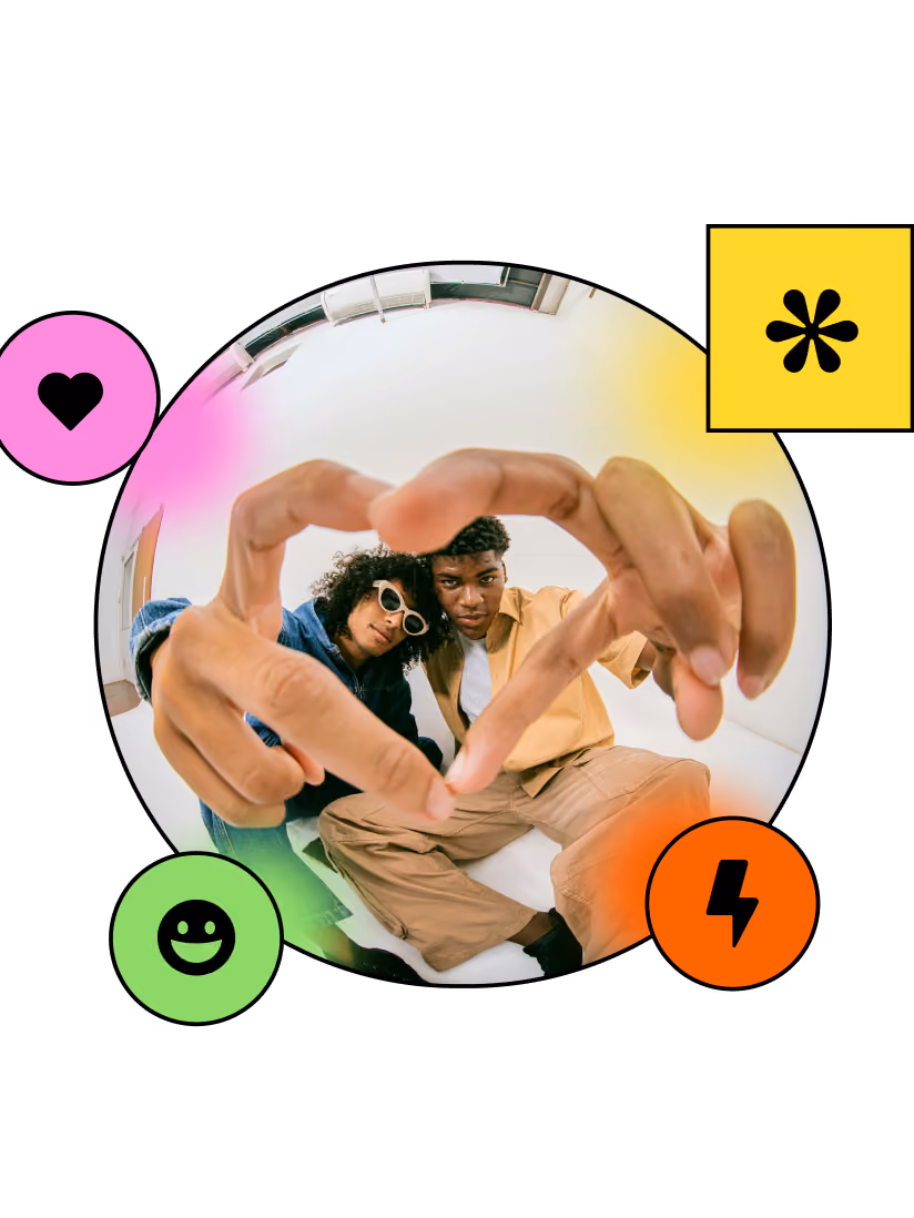 Two people sit close making a heart shape with their hands in a fisheye lens effect.