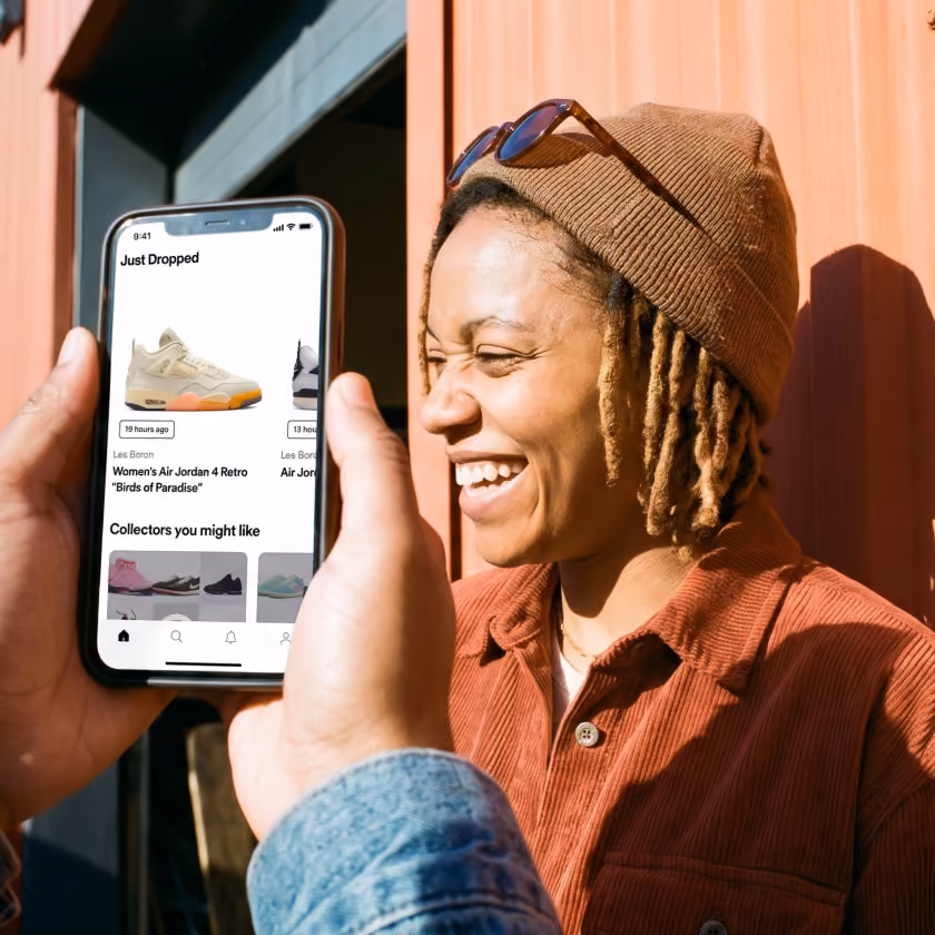 Person holding phone showing 'Just Dropped' sneaker app with Air Jordan 4 retro on screen beside smiling person.