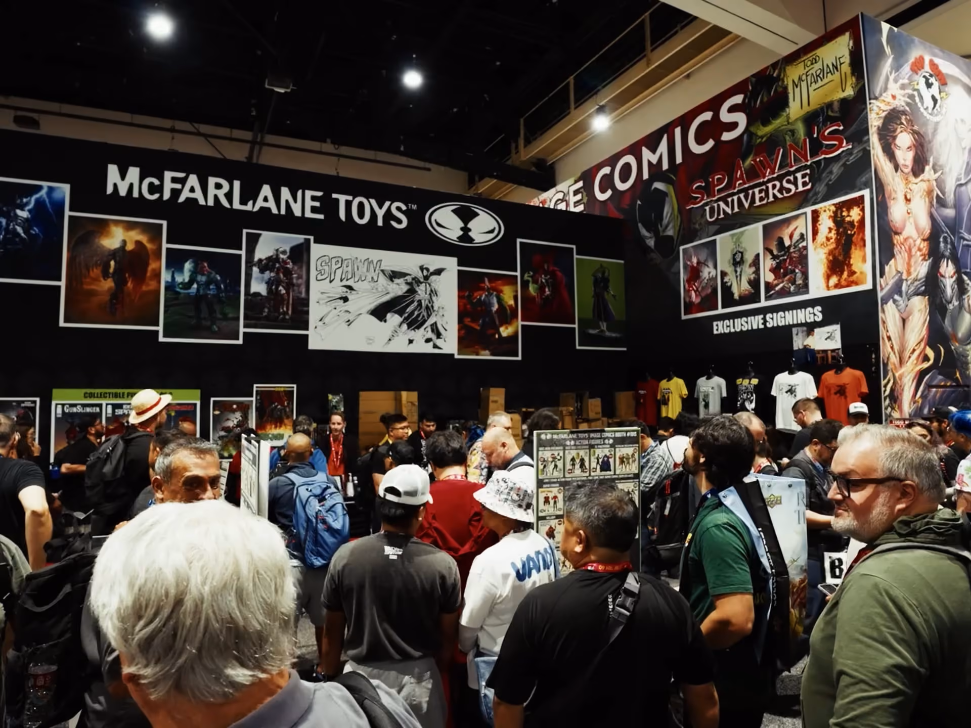 Crowd of people gathered at a convention booth featuring McFarlane Toys and Todd McFarlane's Spawn's Universe with large banners showing comic and toy artwork along the walls.