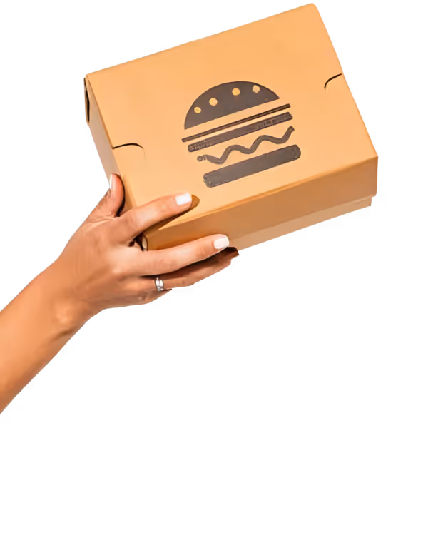 Eine Hand hält eine Burgerverpackung in die Luft. Auf der Verpackung ist ein Burger abgebildet.