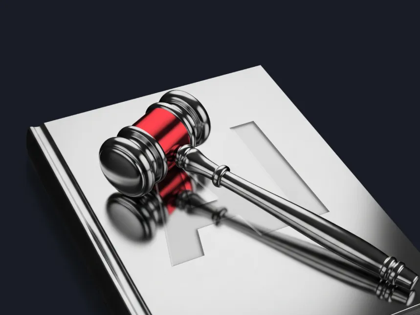 A metallic judge’s gavel resting on a silver book embossed with the letters "AI," representing artificial intelligence legal regulations and digital law.