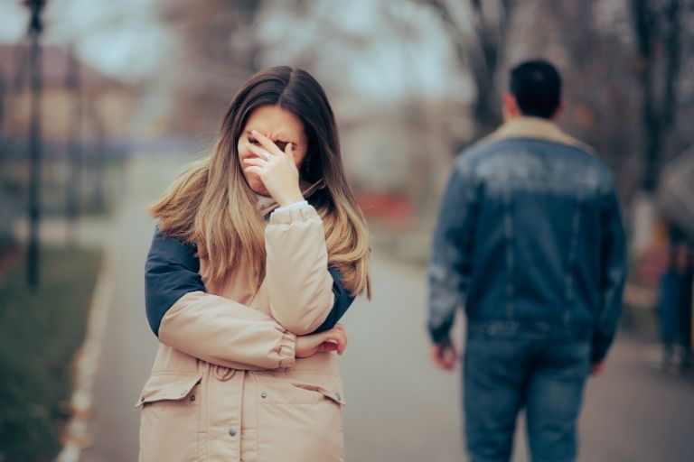 Vrouw verdrietig met hand voor gezicht en weglopende man op achtergrond