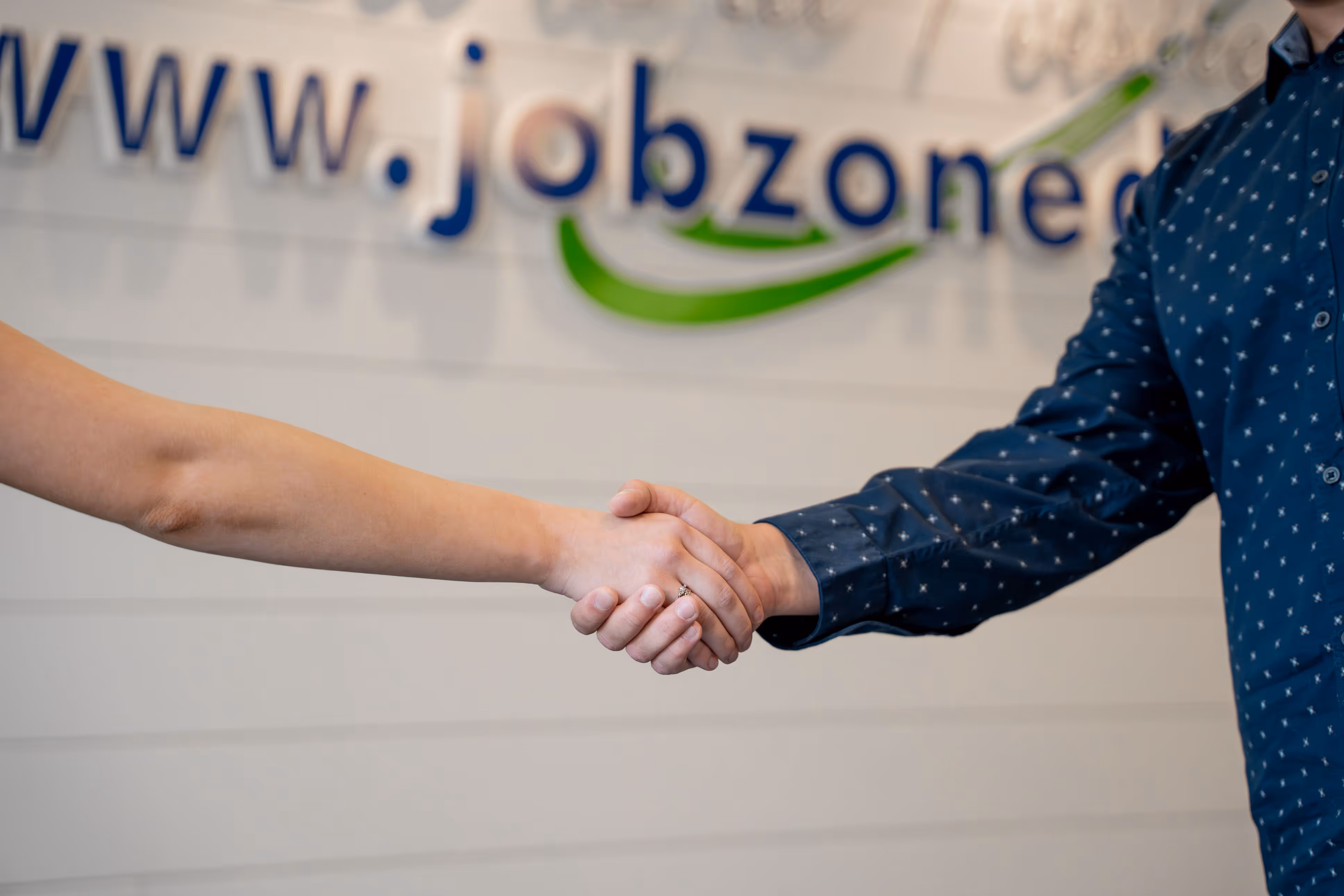 Two people shaking hands in front of a blurred Job Zone d'emploi sign.