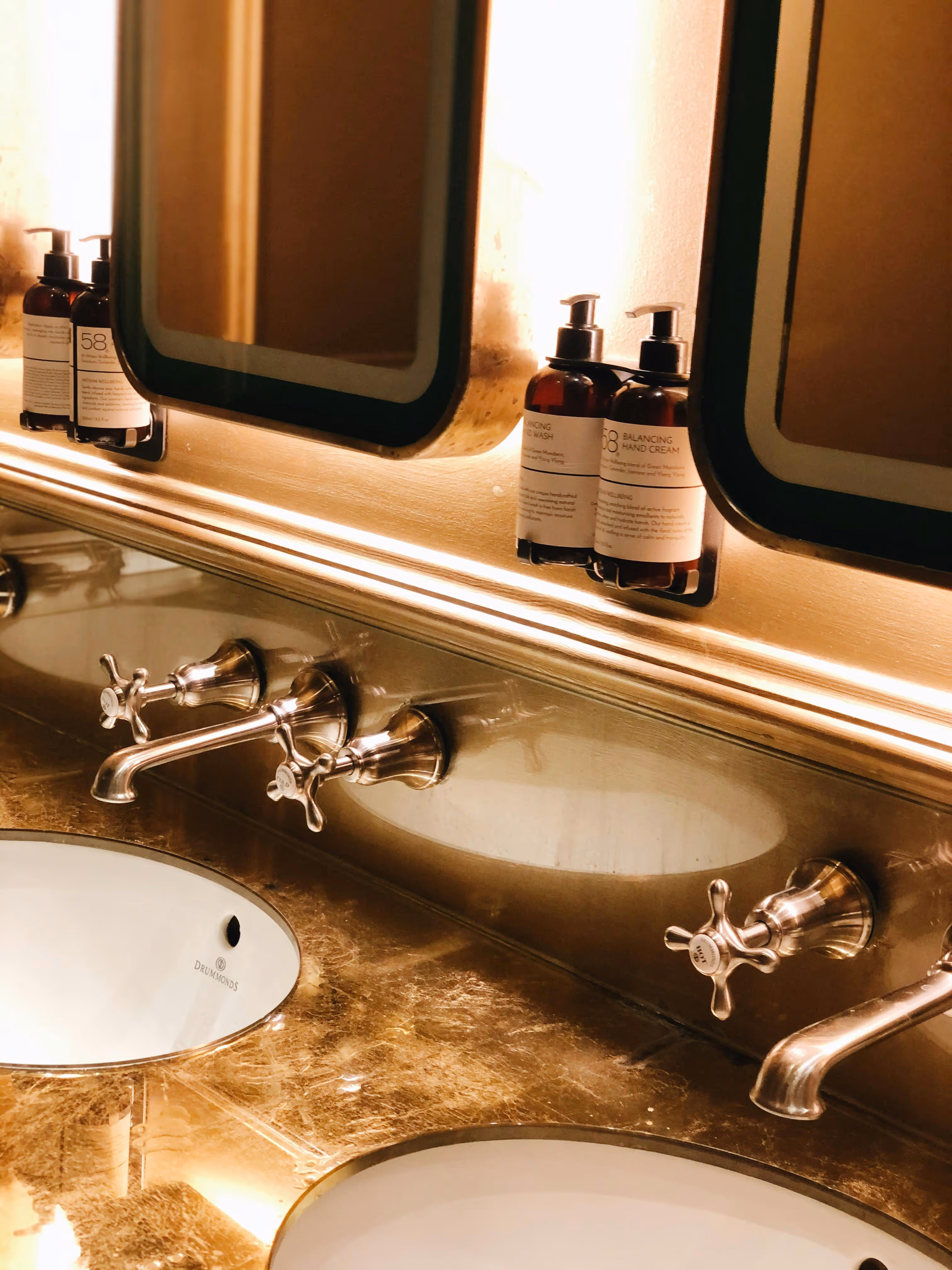 Elegantes Badezimmerwaschbecken mit goldenen Armaturen, Pflegeprodukten und beleuchtetem Spiegel