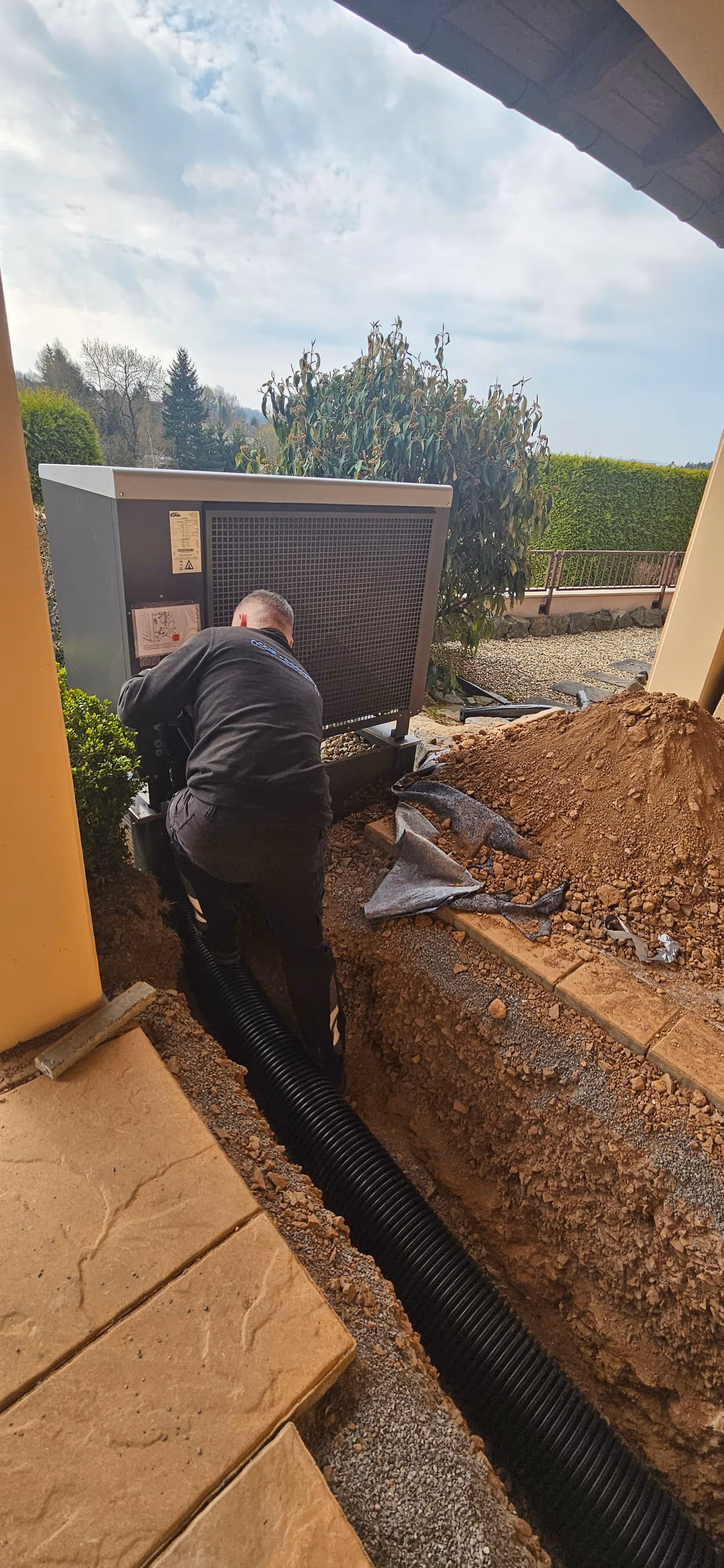 Facharbeiter beim Einbau einer Wärmepumpe im Außenbereich eines Wohngebäudes.