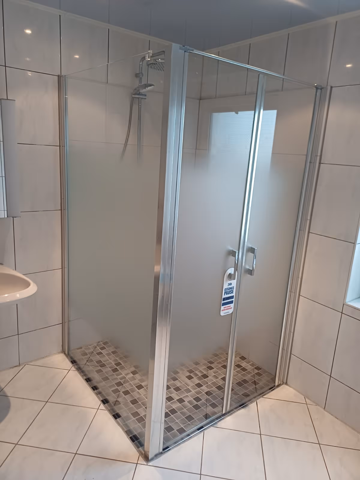 Glasduschkabine mit Mosaikfliesen-Ablauf in gefliestem Badezimmer.