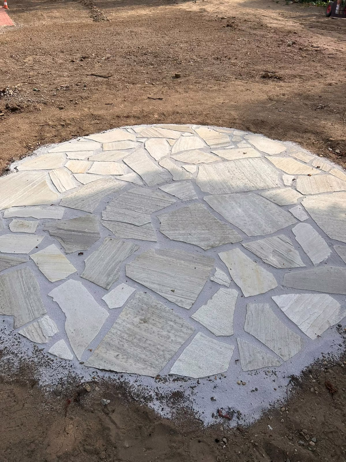 Runde Fläche aus hellen Polygonalplatten, frisch verlegt im Garten