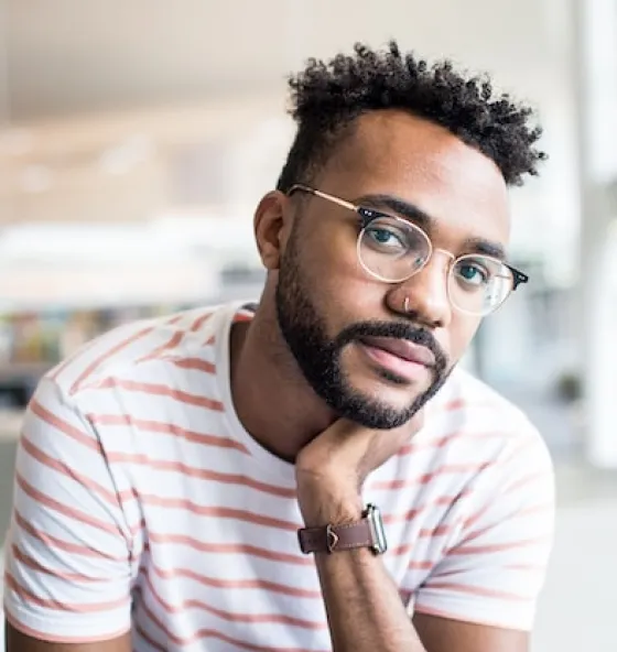Person wearing a striped shirt and watch, sitting with hand on chin in a bright indoor setting.