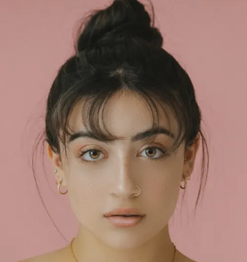 Person with hair in a bun wearing gold earrings against a pink background.