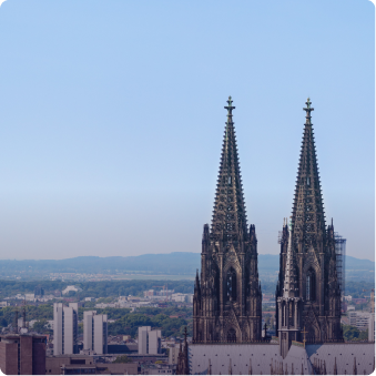 Die beiden gotischen Türme des Kölner Doms vor klarem blauem Himmel, mit der Stadt Köln im Hintergrund.