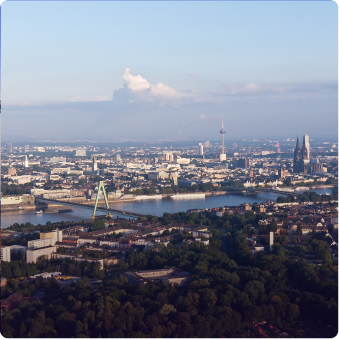 Panoramablick auf Köln mit Rhein, Hohenzollernbrücke, Kölner Dom und Fernsehturm unter blauem Himmel.
