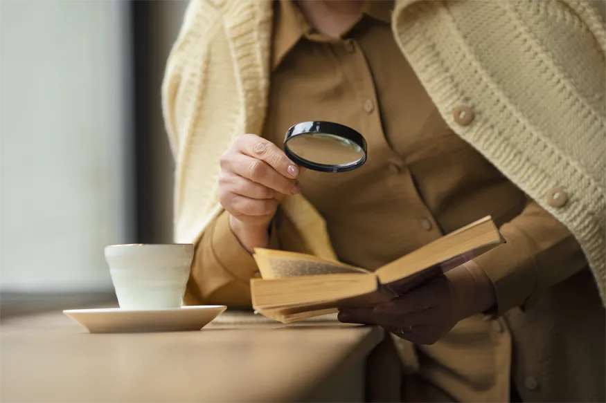 Eine Person nutzt ihre vergrößernde Sehhilfe bzw. Lupe um ein Buch zu lesen nach erfolgreicher Low-Vision-Beratung in Solingen