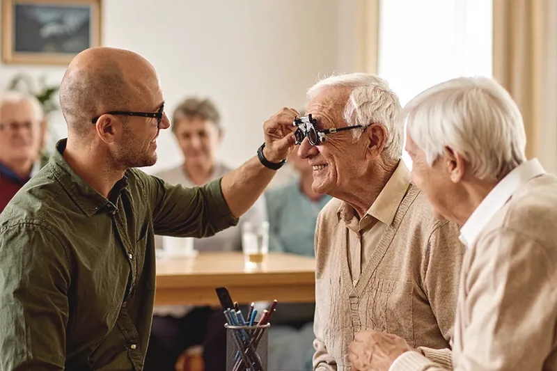 Michael Zuleger reicht einem Senior eine Messbrille für seinen kostenlosen Sehtest