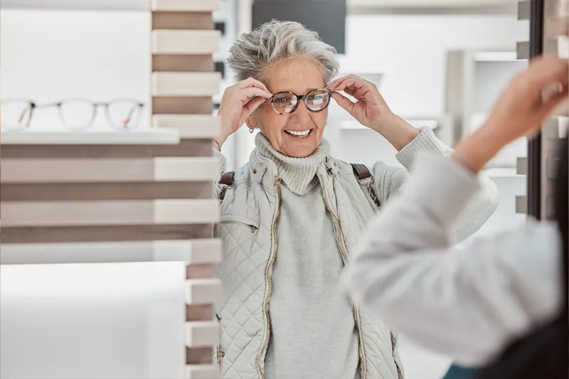 Eine Frau steht vor dem Spiegel und probiert glücklich ihre neue Brille von Brillen Zuleger - Ihrem mobilen Optiker an