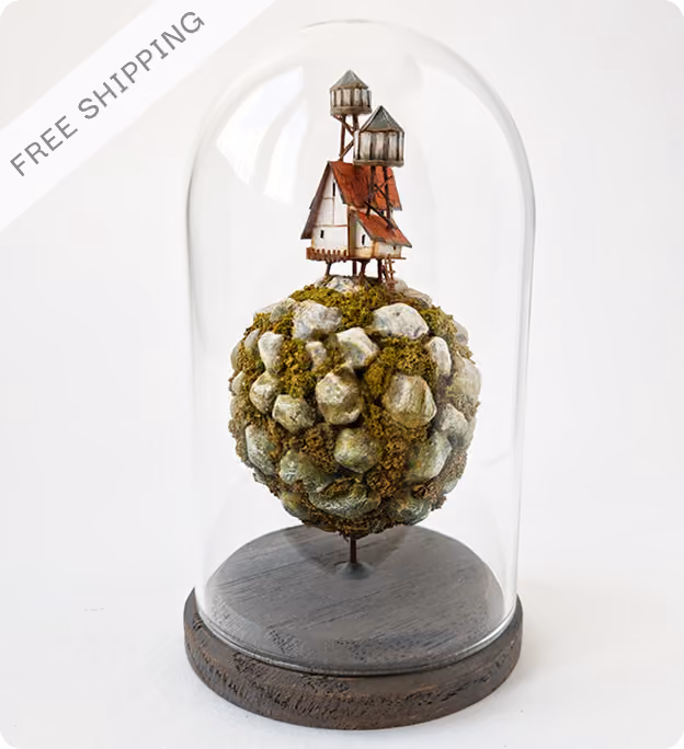 Miniature model of a rustic house with two water towers on a moss-covered rocky sphere, enclosed inside a clear glass dome with a wooden base, labeled with 'FREE SHIPPING' in the corner.