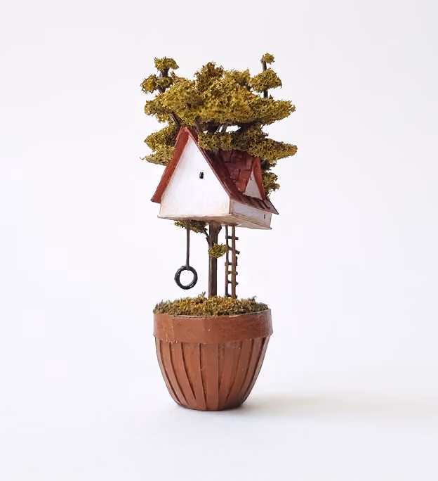 Miniature treehouse with a red roof and white walls built on a tree planted in a brown pot, featuring a small ladder and a tire swing.