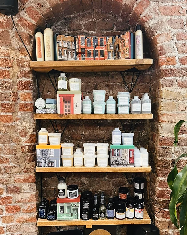 Four wooden shelves mounted on a brick wall holding various skincare and beauty product bottles, jars, and boxes arranged neatly.