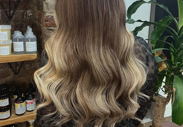 Long wavy hair with a balayage color effect transitioning from dark brown at the roots to blonde at the ends.