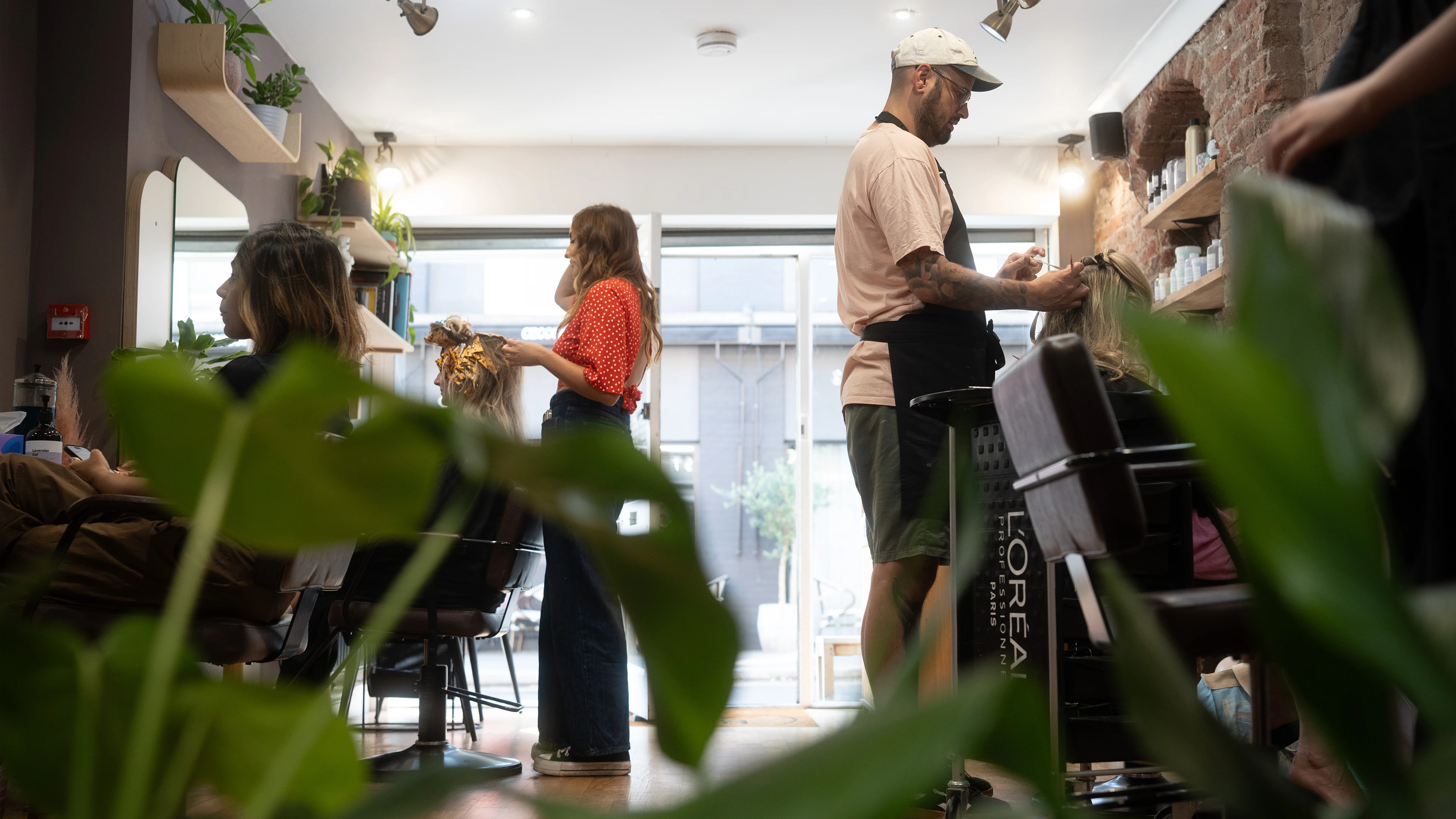 Modern hair salon interior with wooden floor, brown styling chairs, mirrors, brick wall, plants, and wooden door numbered 65.