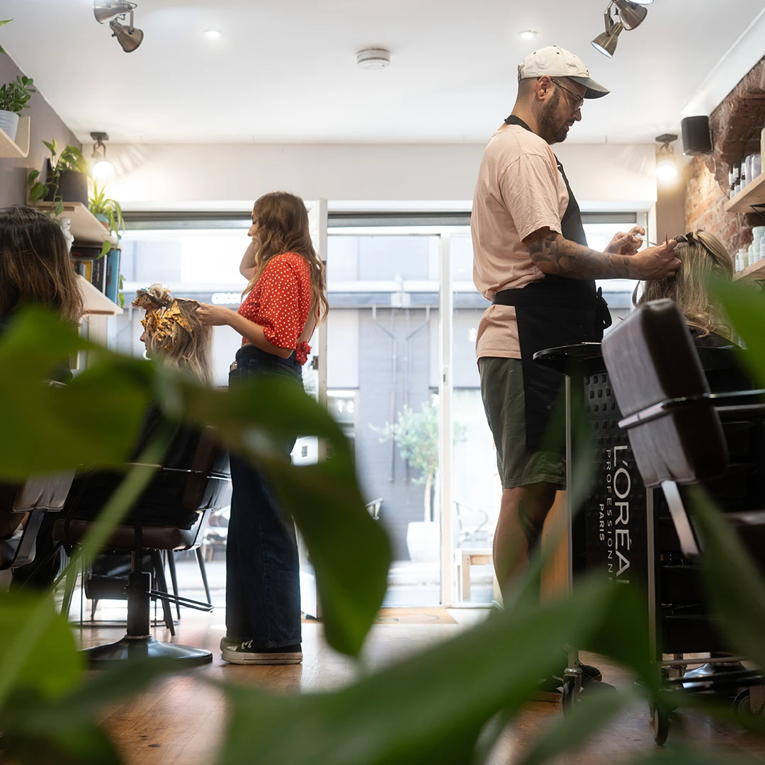 Cozy hair salon interior with brown styling chairs, large mirrors, exposed brick wall, and shelves with hair products.