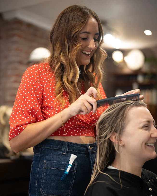 Smiling hairstylist combing a client's wet hair in a salon setting.