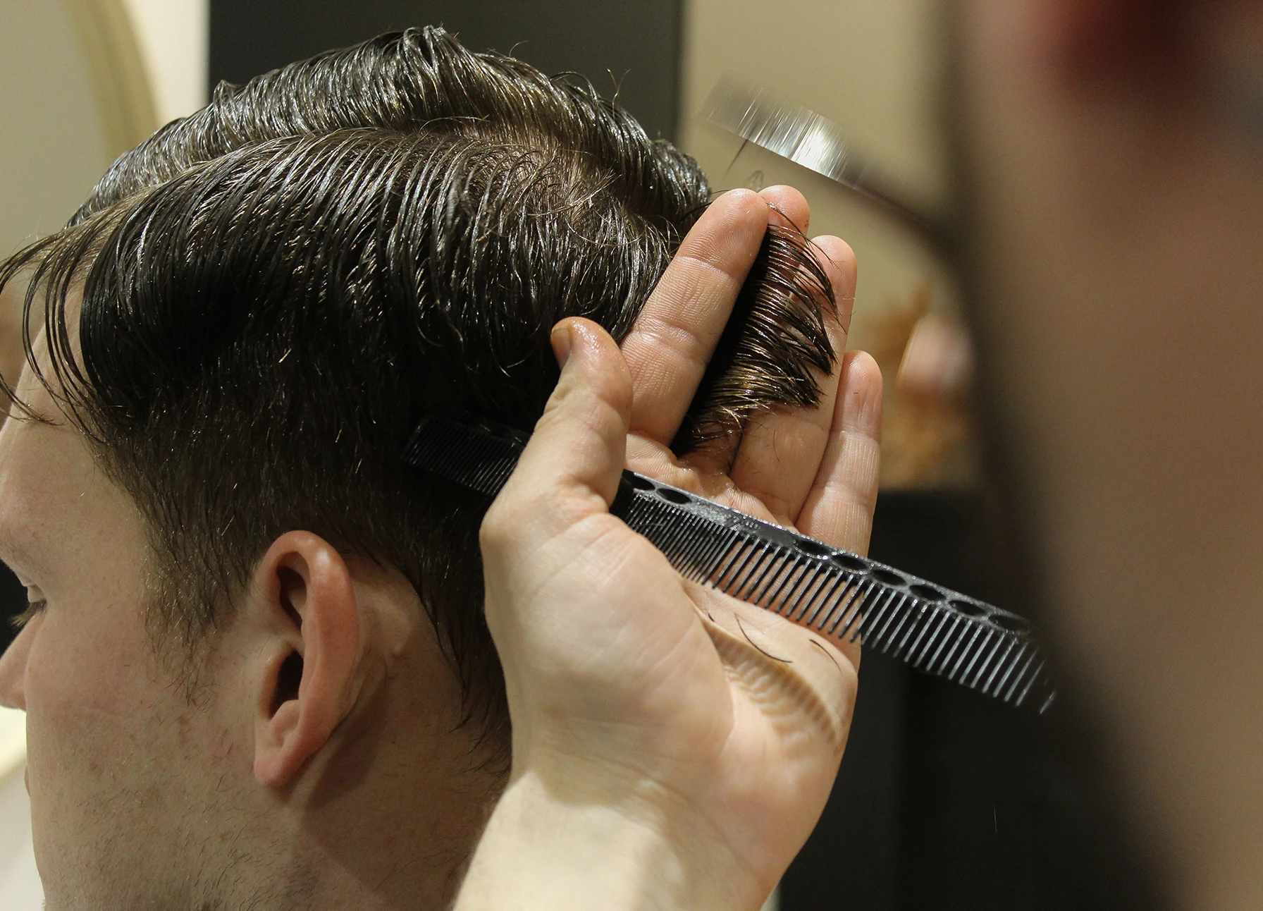 Close-up of a hairstylist holding a comb and a section of wet hair while styling a man's haircut.