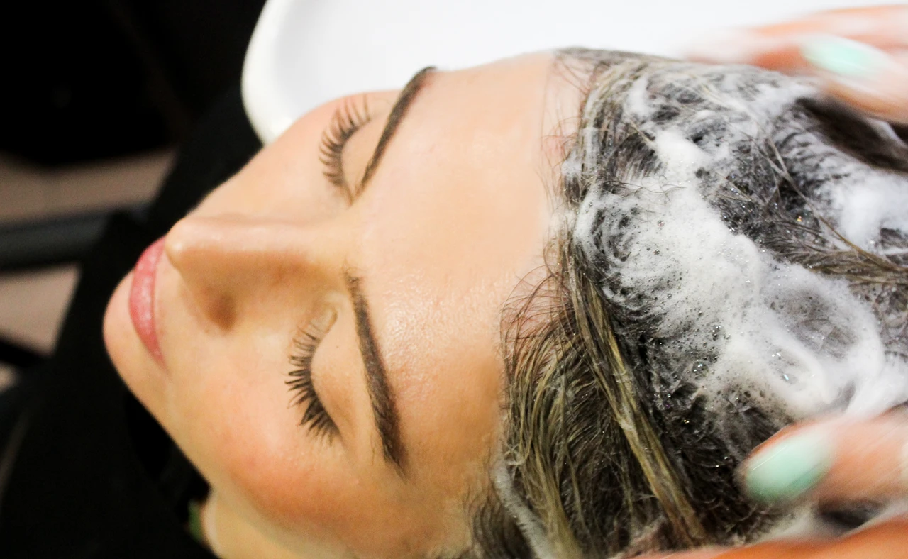 Woman with eyes closed getting shampoo massage on her wet hair with foam at a salon.