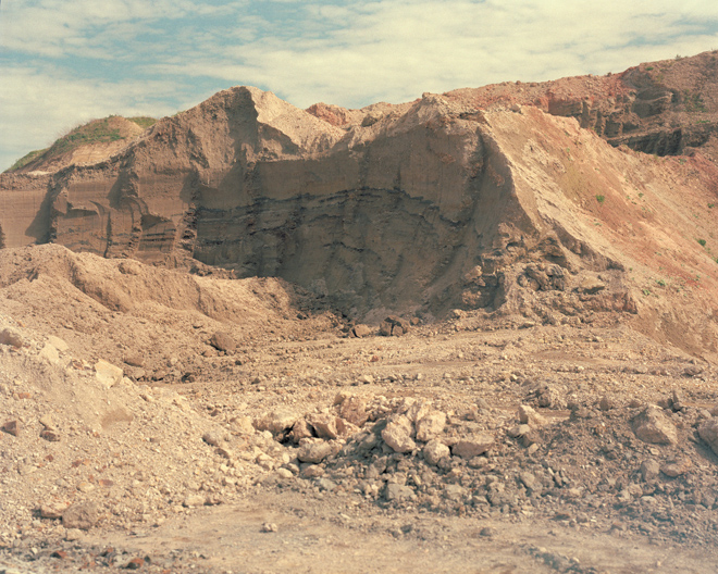 Large dirt mound with visible soil layers under a partly cloudy sky.