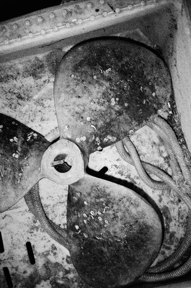 Close-up of a worn, three-bladed metal fan covered in grime and rust inside a mechanical casing.