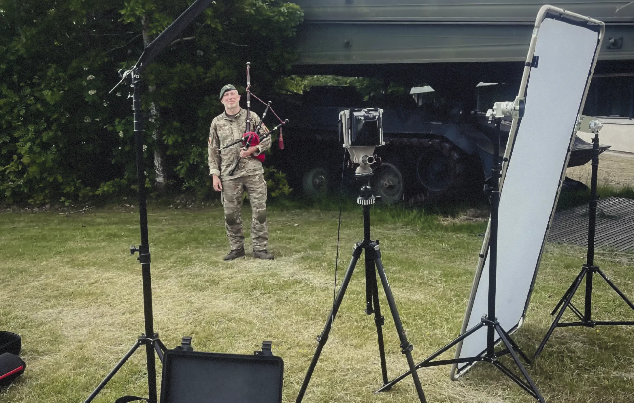 Person in camouflage uniform playing bagpipes outdoors with photography lighting and camera setup.