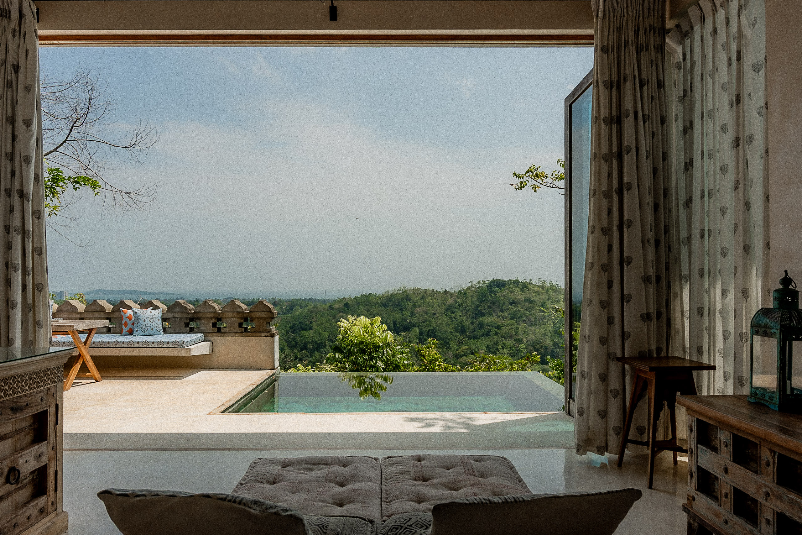 View from a villa through linen curtains to its plunge pool and the jungle-covered hills beyond