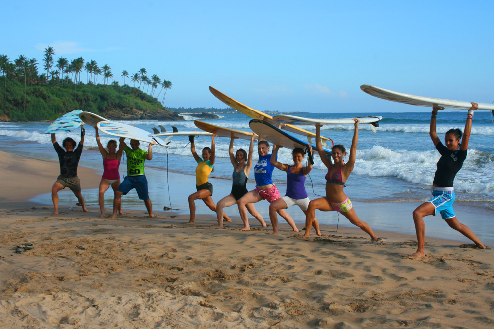 A surf group holding their boards overhead on a palm-fringed beach in Sri Lanka