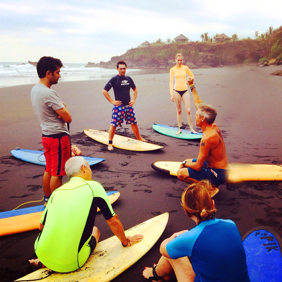 Simon leading a surf lesson on the sand, the group gathered around their boards