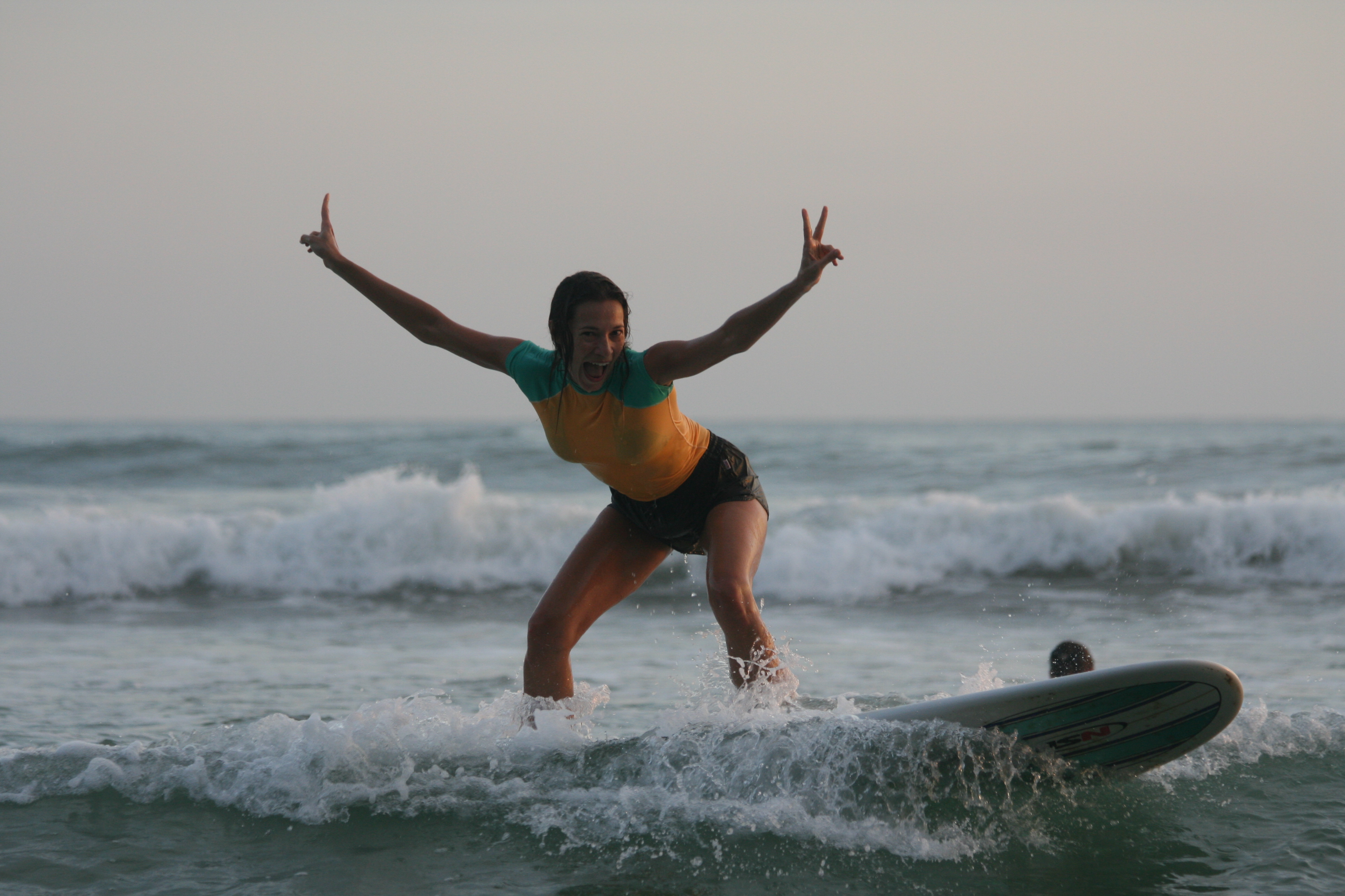 A surfer laughing with both arms raised as she rides a wave in Sri Lanka