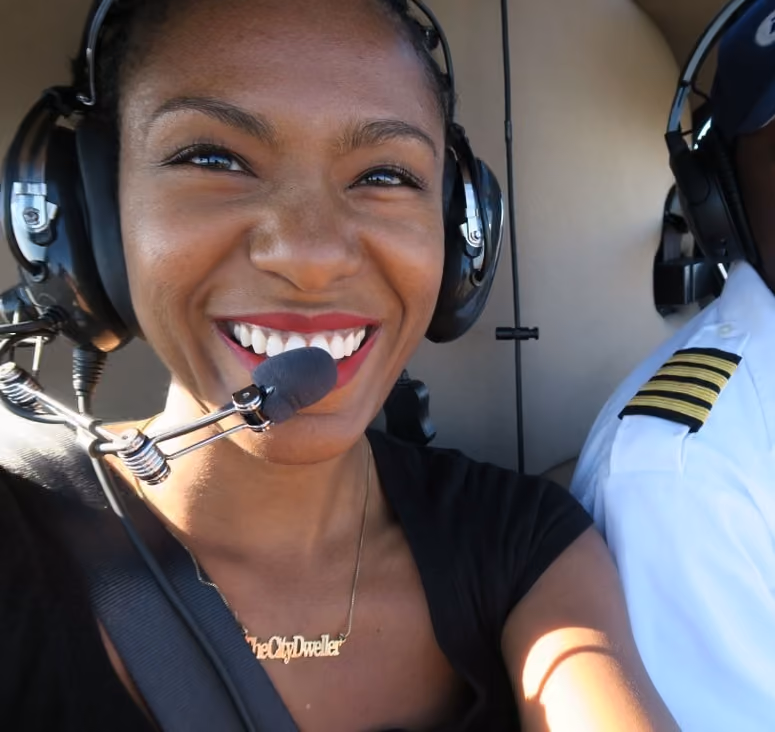 Smiling woman wearing pilot headset with microphone, seated next to a pilot in uniform inside an aircraft.