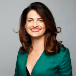 Smiling woman with shoulder-length brown hair wearing a green blazer and red lipstick.