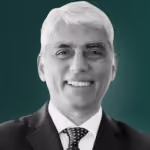 Smiling middle-aged man with short white hair wearing a suit and tie on a green background.