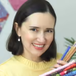 Woman with short dark hair smiling and holding colored pencils near a colorful textile.