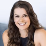 Smiling woman with long brown hair wearing a sleeveless black top against a neutral backdrop.