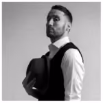 Black and white portrait of a man in a vest holding a hat, looking over his shoulder.