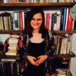 Smiling woman with dark hair standing in front of a bookshelf filled with books.