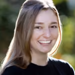 Smiling woman with long light brown hair wearing a black top, with a blurred green natural background.