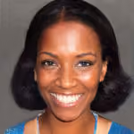 Smiling woman with dark hair styled in a bob wearing a blue top against a gray background.