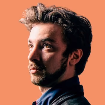 Portrait of a young man with styled dark hair and beard looking to the left on an orange background.