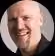 Smiling bald man with beard wearing a black shirt against a dark background.